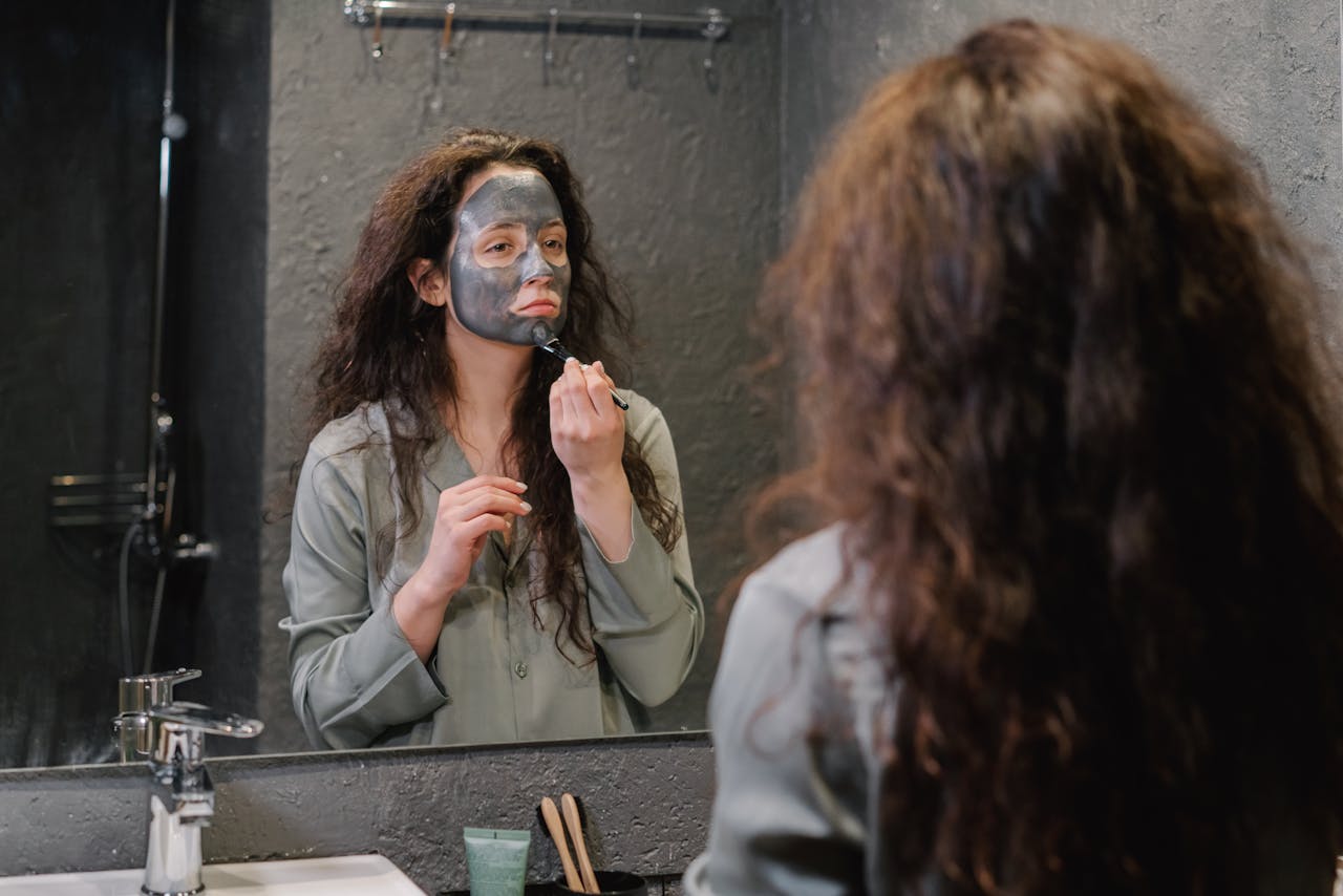 A woman applies a facial mask in the bathroom, focusing on skincare and wellness.