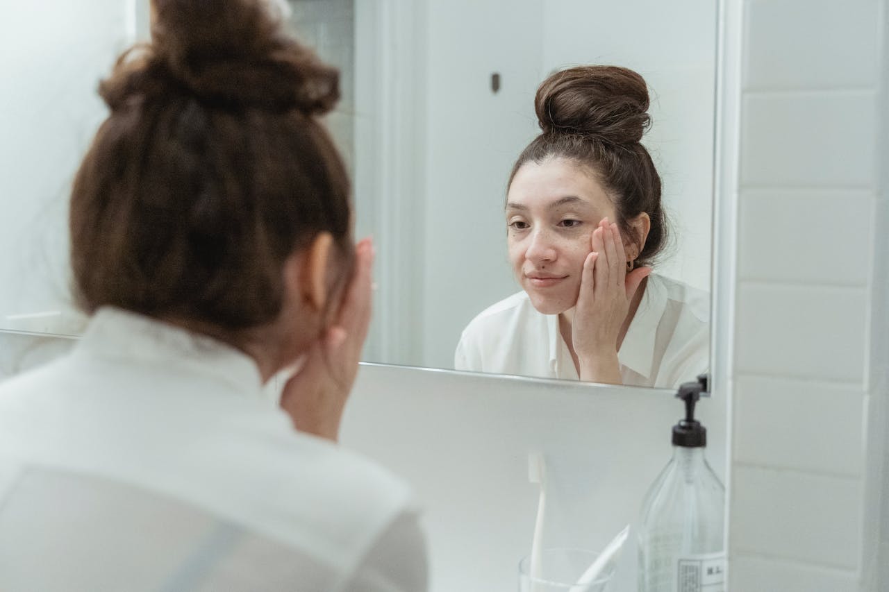 Woman looking at her reflection in the mirror while applying skincare products.